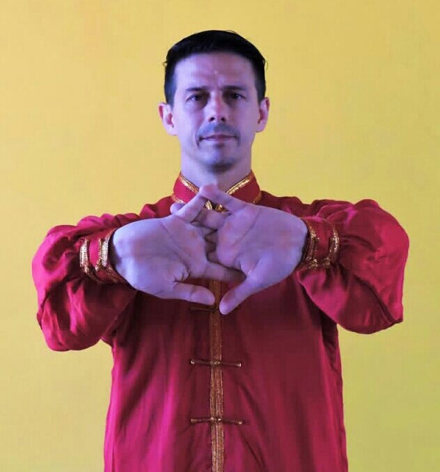 Sifu, de uniforme rojo de Kung Fu, con las manos unidas en el saludo tradicional.